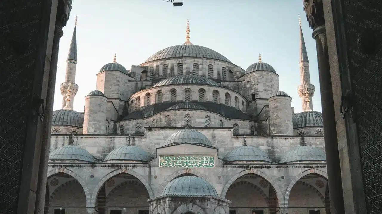 A view of the Blue Mosque in Istanbul, Turkey, showcasing its grand domes and towering minarets framed by an arched entrance.