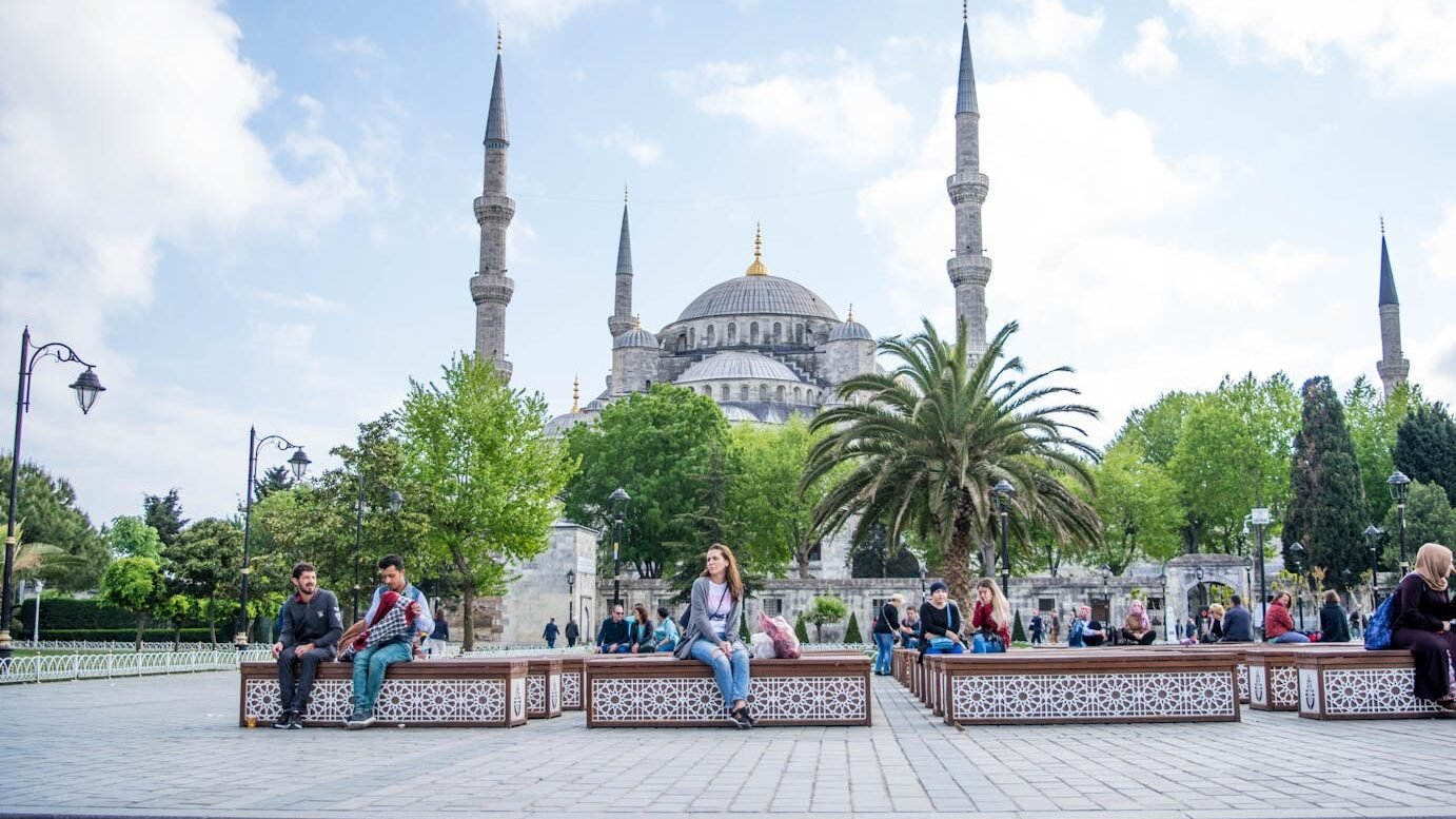 Daytime view of the Blue Mosque in Istanbul with people relaxing in the foreground. A blend of history and daily life.