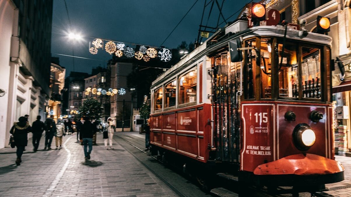 A vibrant night scene in Istanbul featuring a historic tram and festive holiday decorations on a bustling street.