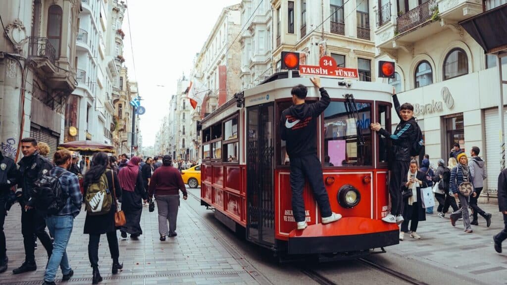 A red tram travels on a street with pedestrians.