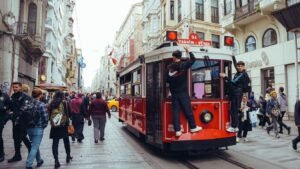 A red tram travels on a street with pedestrians.