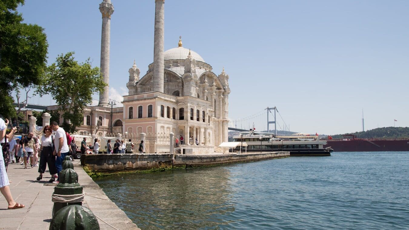 Ortaköy Mosque - a group of people walking on a sidewalk next to a body of water