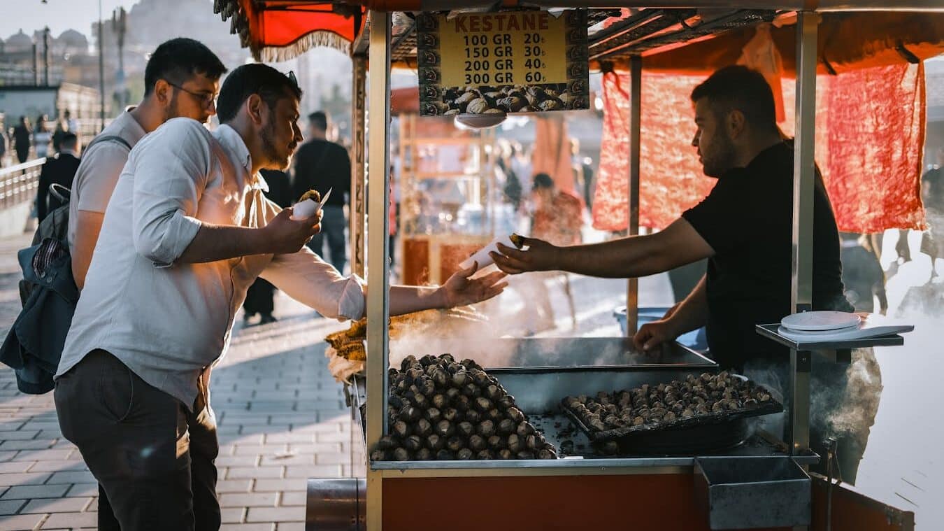 A bustling street market scene with people buying roasted chestnuts in İstanbul.