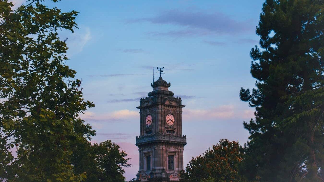 An iconic clock tower amidst trees and a vibrant evening sky in Istanbul, Turkey.
