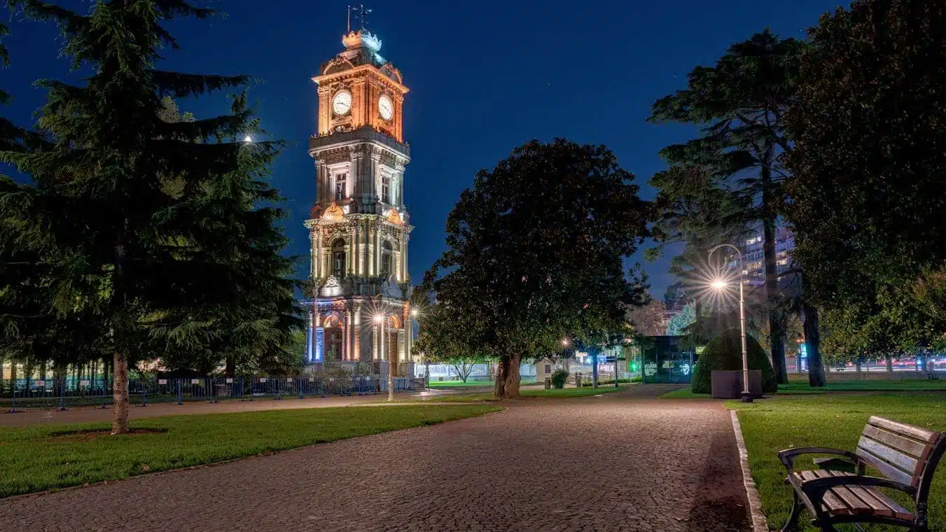 Illuminated Dolmabahçe Clock Tower at night in a tranquil park setting, Istanbul