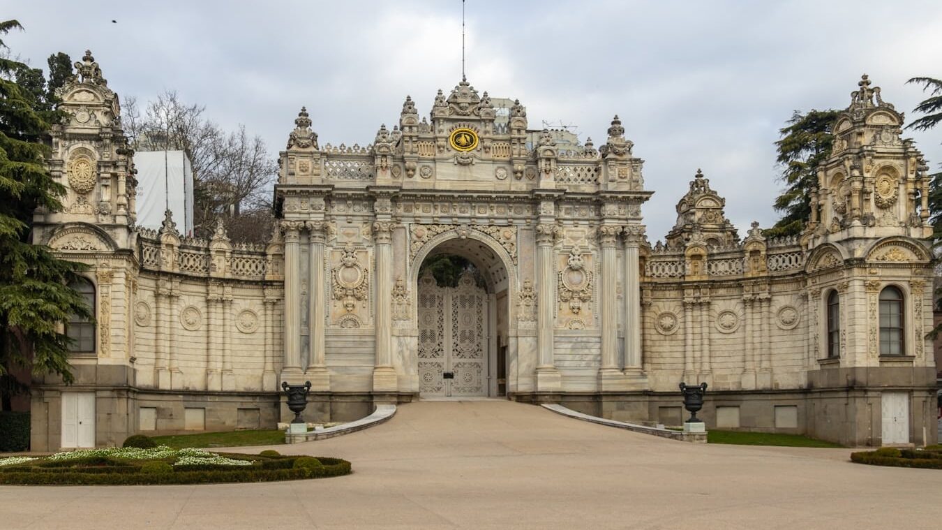 You can enter Dolmabahce Palace with MuseumPass Istanbul. A large stone building with a gate and a clock tower