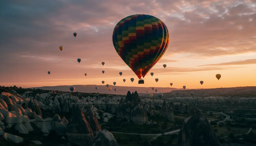 Şafak vakti Kapadokya'nın nefes kesen panoramik manzarası, turuncu ve pembe tonlarında canlı bir gökyüzüyle göz kamaştırıyor. Ön planda, eşsiz peri bacaları ve kaya oluşumlarının dramatik fonunda zarifçe yükselen renkli bir sıcak hava balonu görülüyor. Orta planda ise diğer balonlar nazikçe süzülerek büyüleyici bir atmosfer yaratıyor. Arka planda ise yumuşak, dağınık ışık altında yemyeşil bitki örtüsüyle kaplı tepeler ve vadiler, manzaranın dokularını vurguluyor. Sahne, zengin renkleri ve detayları vurgulayan sinematik bir kaliteyle macera ve huzur duygusunu yakalıyor. Kompozisyon, izleyiciyi Kapadokya'da sıcak hava balonuyla uçmanın bu eşsiz deneyimine daldırarak, balonları çevreleyen görkemli doğal güzelliğe odaklanıyor. Görüntü, son derece detaylı dokuları sergileyen 8K çözünürlükte işlenmiştir. Şafak vakti Kapadokya'nın nefes kesen panoramik manzarası, turuncu ve pembe tonlarında canlı bir gökyüzüyle göz kamaştırıyor. Ön planda, eşsiz peri bacaları ve kaya oluşumlarının dramatik fonunda zarifçe yükselen renkli bir sıcak hava balonu görülüyor. Orta planda ise diğer balonlar nazikçe süzülerek büyüleyici bir atmosfer yaratıyor. Arka planda ise yumuşak, dağınık ışık altında yemyeşil bitki örtüsüyle kaplı tepeler ve vadiler, manzaranın dokularını vurguluyor. Sahne, zengin renkleri ve detayları vurgulayan sinematik bir kaliteyle macera ve huzur duygusunu yakalıyor. Kompozisyon, izleyiciyi Kapadokya'da sıcak hava balonuyla uçmanın bu eşsiz deneyimine daldırarak, balonları çevreleyen görkemli doğal güzelliğe odaklanıyor. Görüntü, son derece detaylı dokuları sergileyen 8K çözünürlükte işlenmiştir.